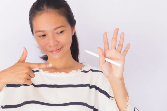 An Asian woman points to her left hand holding a pencil to show that she is left-handed. Left hander day concept.