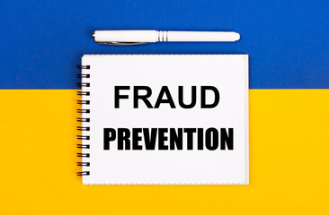A white notebook with the text FRAUD PREVENTION and a white pen on a blue and yellow background.