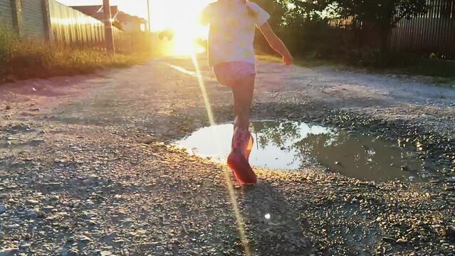 Little girl in rubber boots runs through a puddle on a warm, sunny summer day