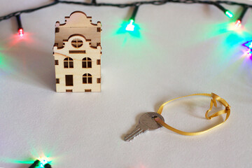 Miniature wooden house with a key and colorful garland. Christmas, New year gift, present. Mortgage, home, real estate, realtor concept. On white background