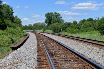 A pair of vacant railroad track bend around a curve in rural northeastern Illinois. The tracks are a main line tangent along with a passing siding on the railway.