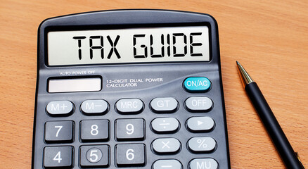 On a wooden table there is a black pen and a calculator with the text TAX GUIDE. Business concept