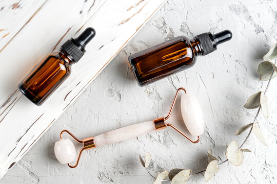 Amber glass bottles with dropper pipette with serum or essential oil and face quartz massage roller on a white concrete background. Skincare cosmetic. Beauty concept for face body care.