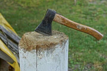 an old iron ax with a comfortable wooden handle sticks out in an old wooden stump against the background of green grass outdoors in summer