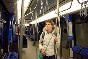 Mature woman in a cabin of subway or tram car. Female passenger of comfortable transport of big city. Urban infrastructure.