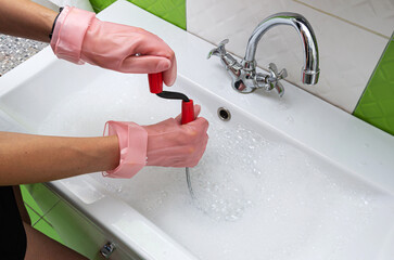 Woman in protective rubber gloves unblocking  a clogged sink with a probe or drained cable at home. 