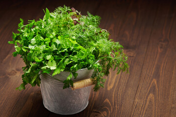 a bunch of green dill, parsley, salad and other greens in an iron bucket, dark wooden background, concept of fresh vegetables and healthy food