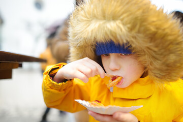 Child eating traditional Poland street food oscypek on Christmas market in Krakow. Oscypek is a grilled cheese of salted sheep milk with different ingredients as bacon or jams. Local cuisine.