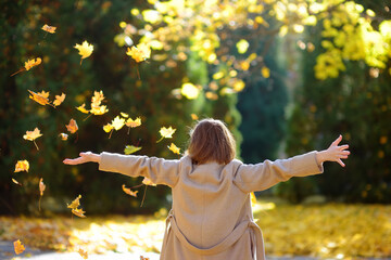 Young woman is having fun while walking through the forest on a sunny autumn day. Girl plays with maple leaves and throws them up. Rustle of leaves.