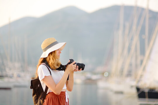 Charming young tourist woman taking a picture on the Mediterranean coast. Attractive red-haired girl photographer with a camera on the background of sea and yachts.