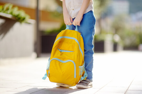 Little student with a backpack near school building. Close-up of child legs, hands and schoolbag of boy standing on staircase of schoolhouse. Back to school concept.