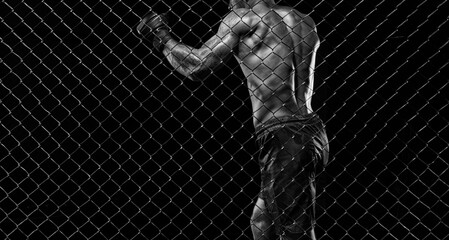 Fototapeta na wymiar Black and white image of a man in a boxing cage. The concept of sports, Muay Thai, martial arts.