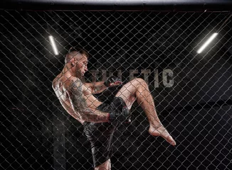 Tuinposter Professional kickboxing fighter trains in a cage ring. The concept of sports, Muay Thai, martial arts. © andy_gin