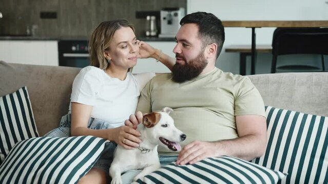 A man and a woman, the owners of a funny Jack Russell Terrier. A married couple in their apartment on the couch.