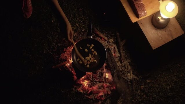 top view movement Video of people cooking garlic frying pan on a camping fire at night.