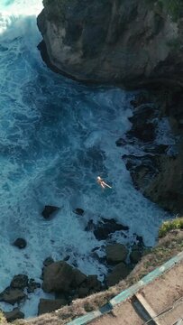 Vertical aerial shot of a person on zip line above splashing seawater