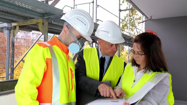 Two men, an architect and construction engineer, foreman and one woman inspect the performance of project, a construction site of a multi-storey house, building in progress
