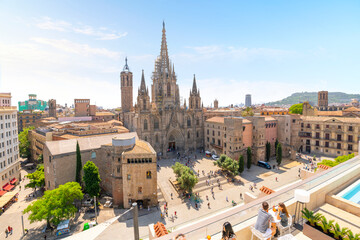 Young couples enjoy drinks with a view of the gothic Barcelona, Spain cathedral from a rooftop terrace with cafe and swimming pool over the Placita de la Seu plaza on a sunny summer day.