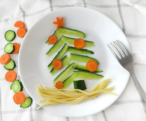 Funny edible Christmas tree made of cucumbers and carrots breakfast idea for kids food. Top view of the Christmas background. holiday, celebration, food art concept
