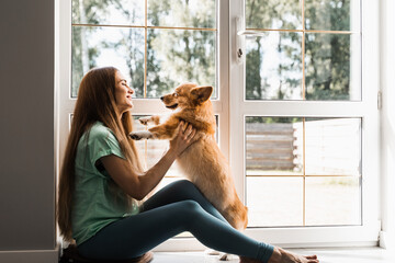 Attractive girl hug and play with corgi dog at home. Welsh Corgi Pembroke with his owner woman on...