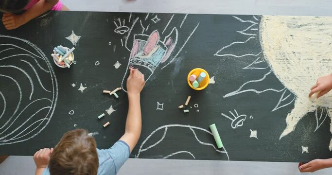 Group of creative little boys and girls drawing a picture of outer space in a preschool classroom from a top view. A young class of kindergarten kids, students or learners doing an artwork