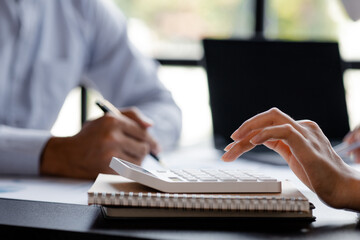 A businessman is using a white calculator to calculate financial numbers, he is sitting in his...