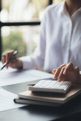 A businessman is using a white calculator to calculate financial numbers, he is sitting in his...