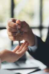 A home rental company employee is handing the house keys to a customer who has agreed to sign a rental contract, explaining the details and terms of the rental. Home and real estate rental ideas.