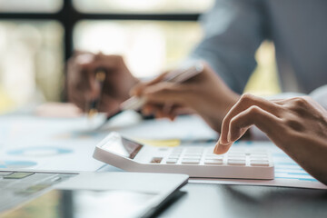 A businessman is using a white calculator to calculate financial numbers, he is sitting in his...