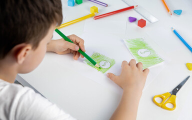 A little boy enthusiastically draws toy money with colored pencils for the game. Selective focus. Family budget. Economy. Money. The kid draws. Economic crisis. Kids play.