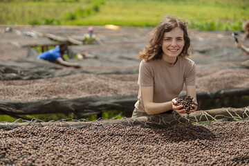 Smiling lady holding dried coffee beans in hands at farm in Africa region with workers on the...