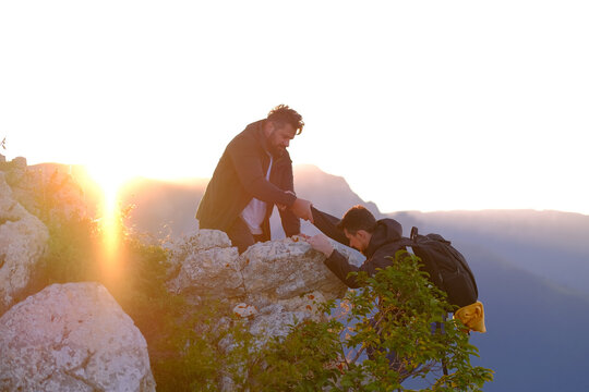 Hiking team helping each other friend giving a helping hand while climbing up on the mountain rock at sunrise. Adventure travel. Extreme sports outdoor. 
