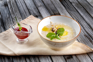 Porridge with pine nuts, decorated with mint leaves. There is jam next to it.