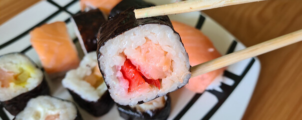 Sushi sticks in hands and set of rolls on plate. Delicious sushi with sliced rice and fresh...