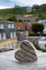Obraz na płótnie Canvas French heartshaped neufchatel cow cheese on white paper and view on old houses of Etretat, Normandy, France