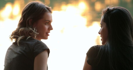 Young women speaking by lake. Two female friends in conversation exchanging ideas at sunset
