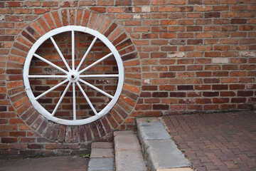 texture background of brick wall and old vintage carriage wheel painted white with copy space 