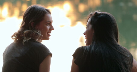 Friends talking by a lake. Girlfriends exchanging ideas and in conversation speaking to one another outdoors in nature