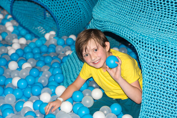happy joyful little boy playing in a dry pool with plastic balls	
