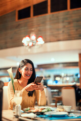 latin young woman sitting in cafe or restaurant using smartphone and smiling happily portrait 