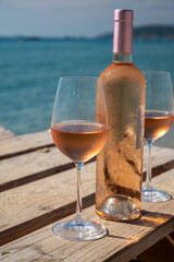 Glasses and bottle of cold rose wine from Provence served outdoor on wooden yacht pier with view on blue water and white sandy beach Plage de Pampelonne near Saint-Tropez, France