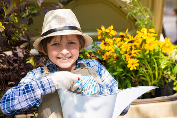happy boy in a hat, apron, holding a watering can in a green garden
