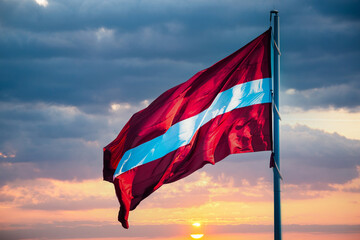 Flag of the Republic of Latvia. Latvian flag waving in the wind against the beautiful sunset - obrazy, fototapety, plakaty