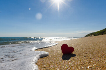 Little heart on the seashore. Sea wave and wooden heart on the sand. Selective focus on the heart.