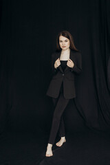 A girl in a black suit stands on a black background