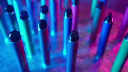 Lots of E-Cigarettes and Vapes with Smoke in Neon Lighting. Concept of Bad Habits. Modern Smoking Electronic Cigarettes. Slow Motion