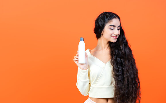 Beautiful indian ethnicity woman admiring her long, healthy hair thanks to the white blank shampoo bottle she demonstrates.