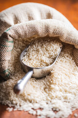 Uncooked white rice in burlap sack on wooden table.