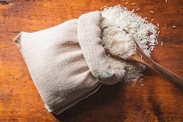 Fototapeta na wymiar Uncooked white rice in burlap sack on wooden table.