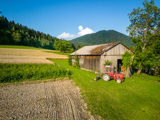 Czerwony traktor przed stodołą w górach - obrazy, fototapety, plakaty